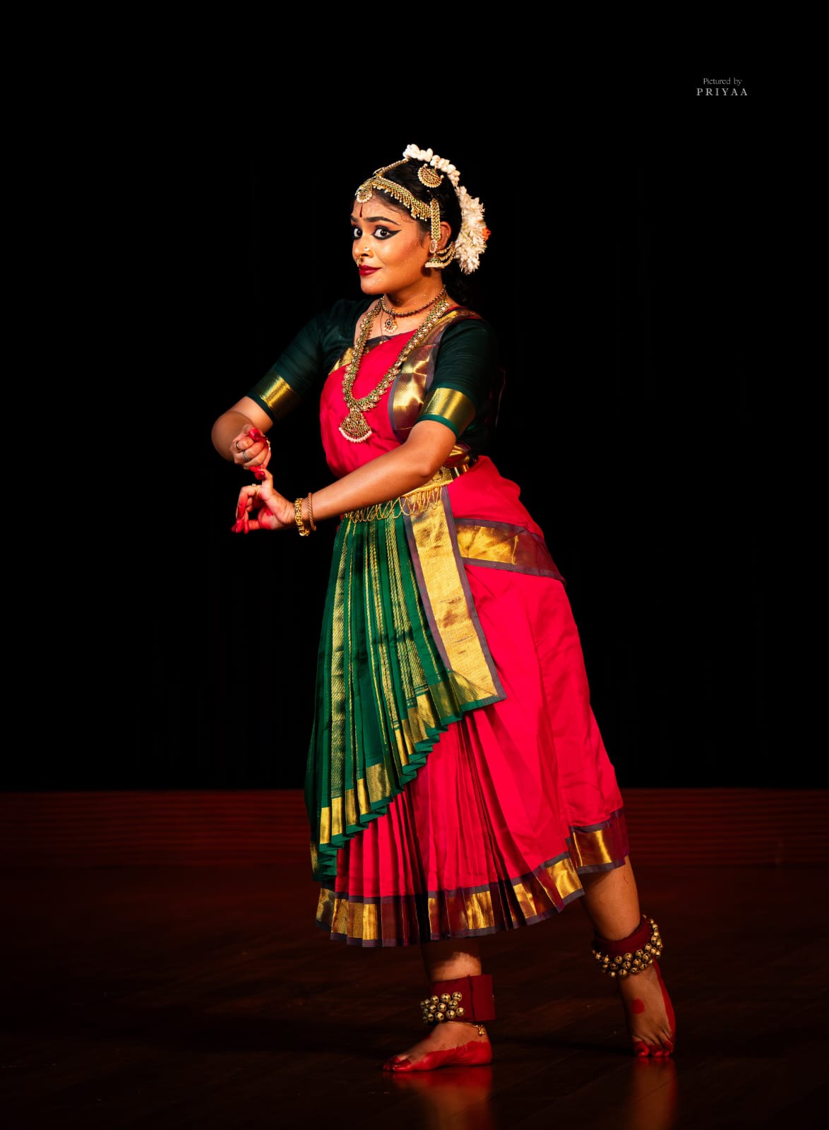 Bharatanatyam dancer in a red and green silk costume, mid-gesture on stage