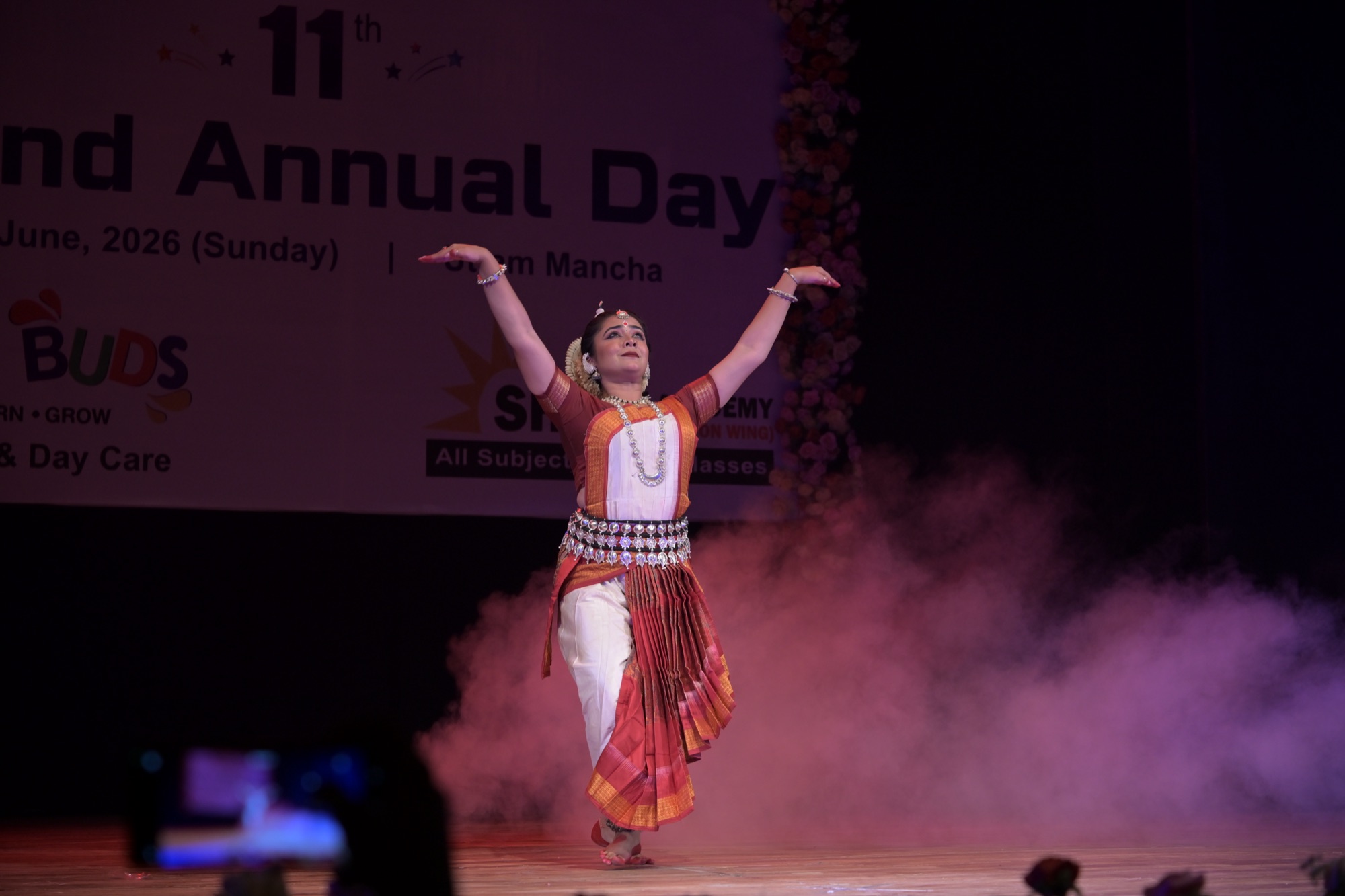 Odissi dancer with arms raised skyward amid stage smoke